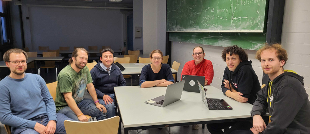 Seven members of Theoretical Physics I around a table with laptops in a seminar room, blackboards in the background